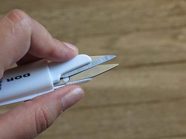 Белые ножницы для обрезки ниток в пальцах на фоне деревянного стола