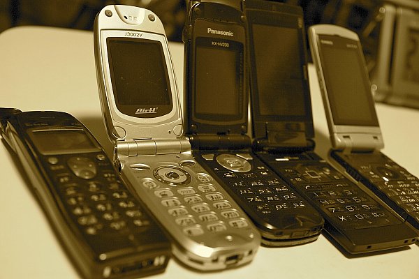 Пять японских телефонов-раскладушек на столе, в центре серебристая модель с открытой крышкой